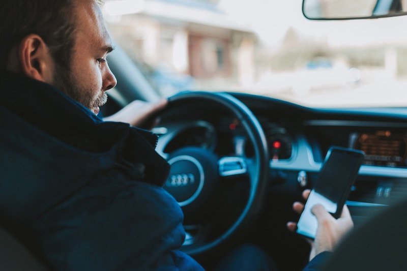 man behind wheel of a car texting